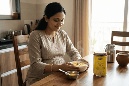 Pregnant woman at home with a spoon of golden A2 bilona ghee on a wooden table, morning light, clay curd pot and steel milk can in background.